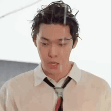 a young man in a wet shirt and tie is standing in the rain .