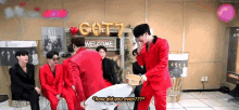 a group of men in red suits are sitting around a table and talking .