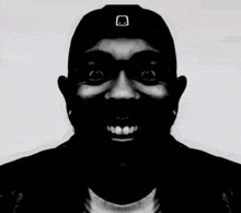 a black and white photo of a smiling man wearing a hat .