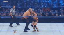 two men are wrestling in a wrestling ring with a referee and a crowd watching ..
