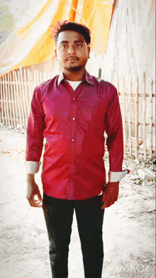 a man in a red shirt and black pants stands in front of an orange tarp
