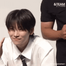 a man in a black shirt with the word team on it stands behind a boy in a white shirt and tie