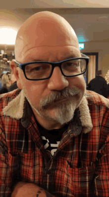 a man with glasses and a beard is wearing a plaid shirt with the letter t on it