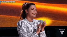 a woman in a white dress is smiling and clapping her hands while sitting on a stage .