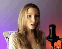 a woman sitting in front of a microphone with a purple background