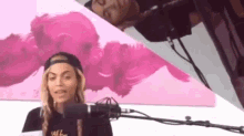 a woman in a baseball cap is standing in front of a microphone in front of a pink painting .