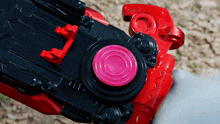 a close up of a red and black toy with a pink button