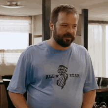 a man with a beard wears a blue shirt that says all star