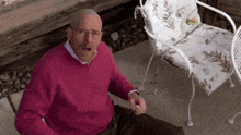 an older man in a pink sweater is sitting on the ground