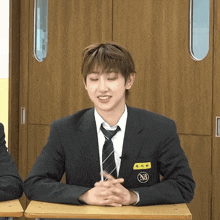 a man in a suit and tie with a name tag that says nb sits at a desk