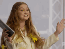 a woman in a white jacket with yellow flowers in her hair holds a remote control