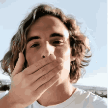 a man with long hair covering his mouth with his hands