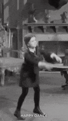 a little girl is dancing in a room with the words `` happy dance '' written below her .
