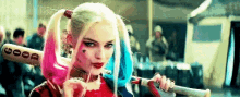harley quinn from suicide squad is holding a bat and a lollipop .