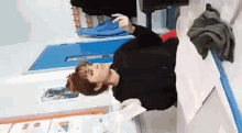 a woman in a black jacket is sitting on a table with a piece of paper in her hand .