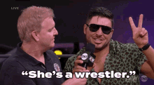 a man holding a microphone with the words " she 's a wrestler " on it