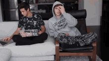 a man wearing a los angeles hoodie sits on a couch next to another man