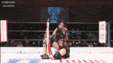 a woman in a wrestling ring holds a trophy with the word stardom on the bottom