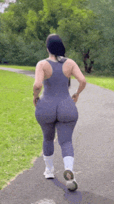 a woman in a gray jumpsuit is walking down a path .