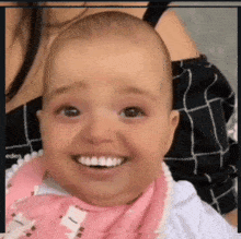 a baby wearing a pink bib is smiling with a woman behind him