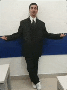 a man in a suit and tie is standing with his arms outstretched in front of a blue wall .