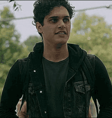 a man with curly hair is wearing a denim jacket and a black shirt .