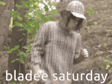 a man wearing a plaid shirt and a hat is standing in the woods with the words bladee saturday written below him