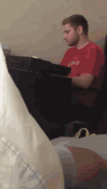a man in a red shirt is sitting at a keyboard