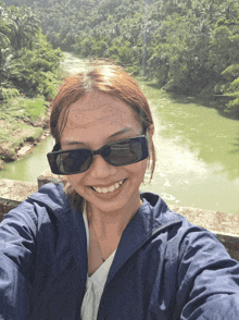 a woman wearing sunglasses takes a selfie with a river in the background