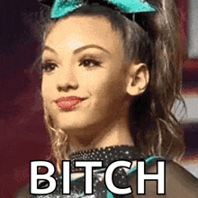 a cheerleader is wearing a blue bow and the word bitch is on her face .