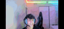 a young man wearing headphones and a microphone is sitting in a room with a rainbow light on the ceiling .