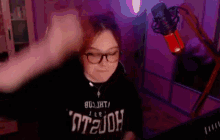 a woman wearing glasses and a black shirt is standing in front of a microphone in a room .