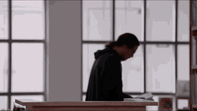 a man in a blue hoodie sits at a desk in a library