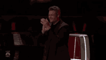 a man in a suit is applauding while sitting in front of a microphone .