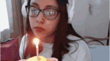 a girl wearing glasses is blowing out a candle on a cake .