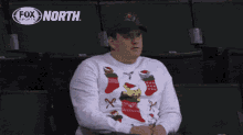 a man wearing an ugly christmas sweater is sitting in a fox north stadium