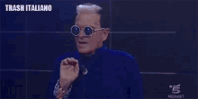 a man wearing sunglasses and a blue shirt is making a funny face on a stage .