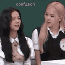 two girls are sitting next to each other in front of a green board and the word confusion is on the bottom of the screen .