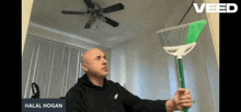 a man holding a green broom with the name halal hogan on the bottom right
