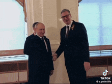 two men shaking hands in front of a window with tiktok written on the bottom right