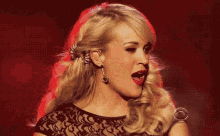 a woman wearing a black top and earrings smiles in front of a red background