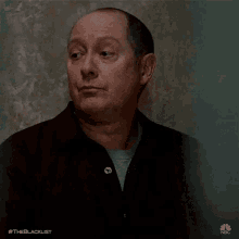 a man in a black shirt is looking up at something while standing in front of a wall .