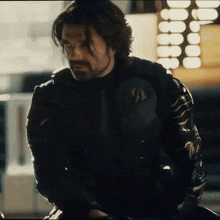 a man with long hair and a beard is wearing a black jacket with an arrow on it
