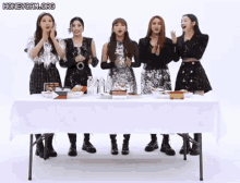 a group of girls are standing around a table with a white tablecloth .