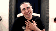a man wearing glasses and a black shirt with the letter g on it smiles