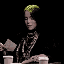 billie eilish is holding a piece of paper while sitting at a table .