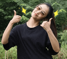 a woman wearing sunglasses and a black shirt gives two thumbs up