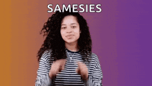 a woman with curly hair is wearing a striped shirt and making a gesture with her hands .