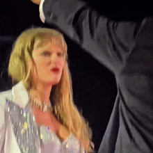 a woman in a white jacket and silver top is standing next to a man in a suit