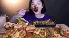 a woman is eating a sandwich with chopsticks while sitting at a table filled with food